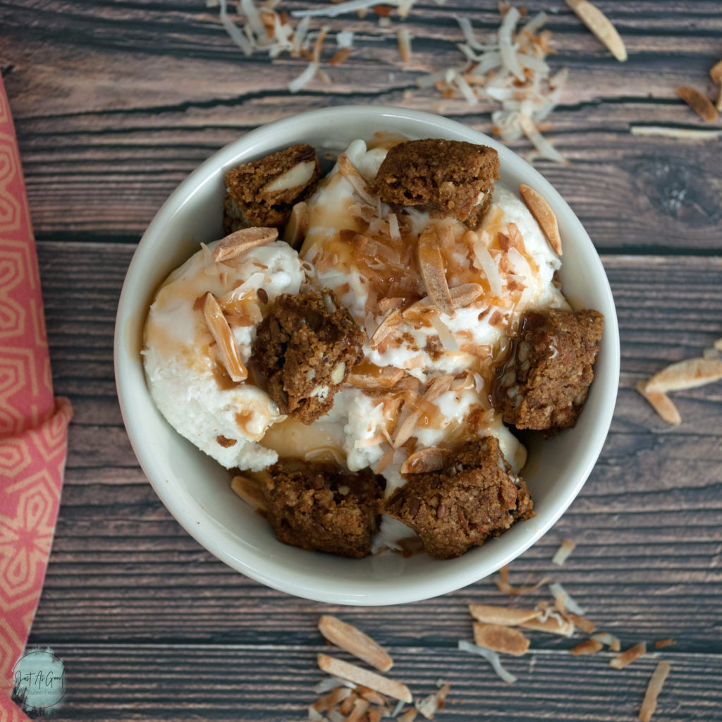 Bowl of coconut ice cream with coconut, almonds, caramel sauce and carrot cake bar