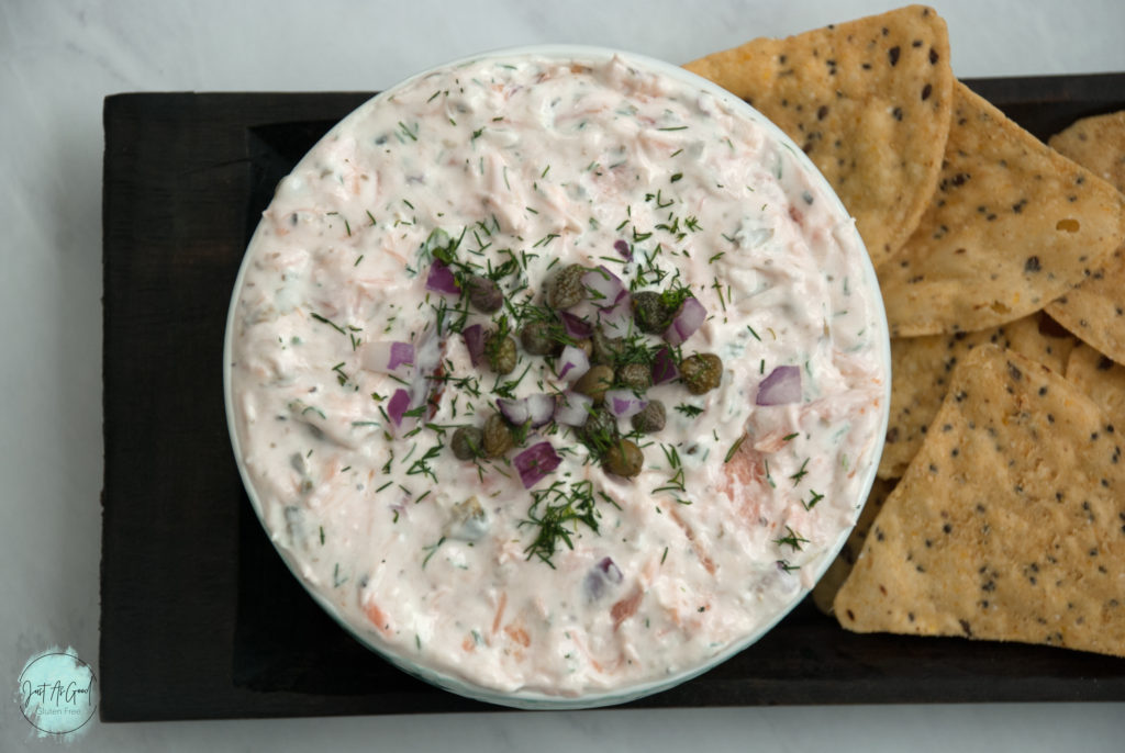 bowl of smoked salmon dip topped with capers, red onion and dill, with seeded tortilla chips