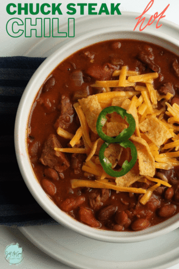 bowl of red chili topped with cheddar cheese, fritos and jalapeno