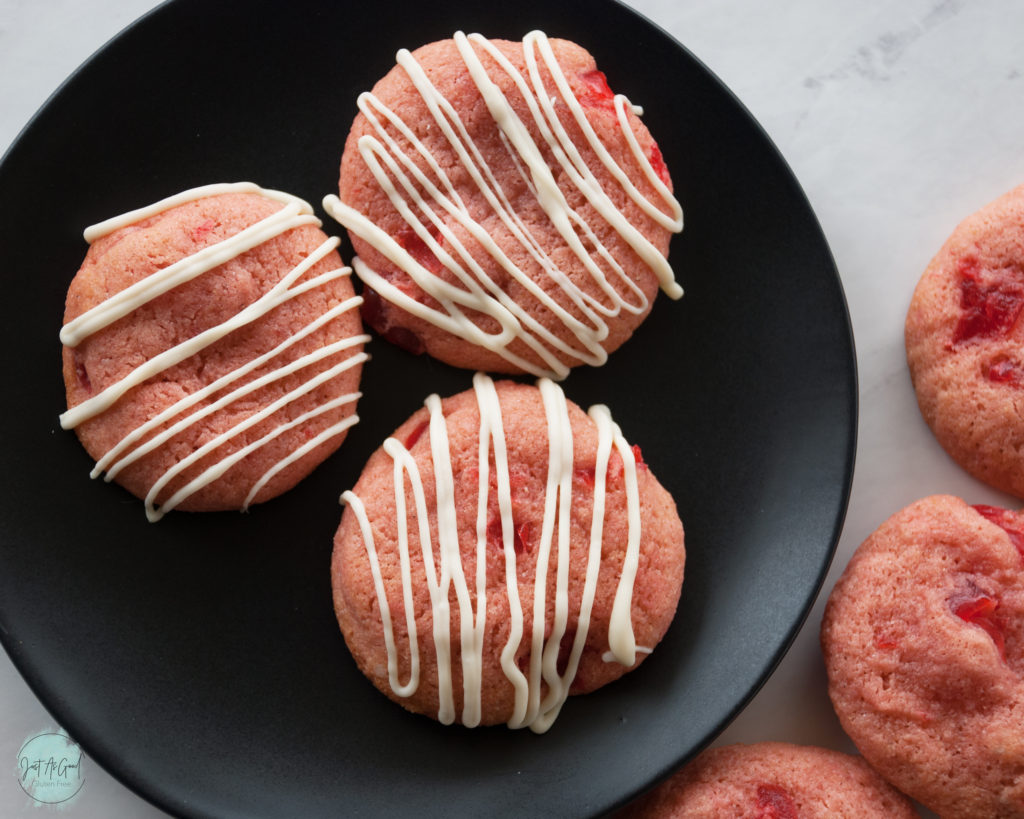 Trio of cherry cookies with white chocolate drizzle on a black plate