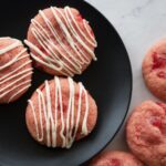 Trio of cherry cookies with white chocolate drizzle on a black plate