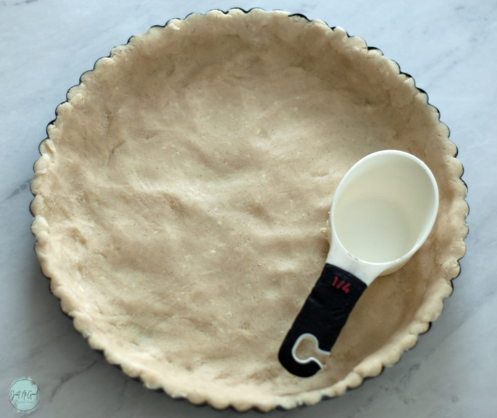 gluten free dough pressed into tart pan using measuring cup to flatten