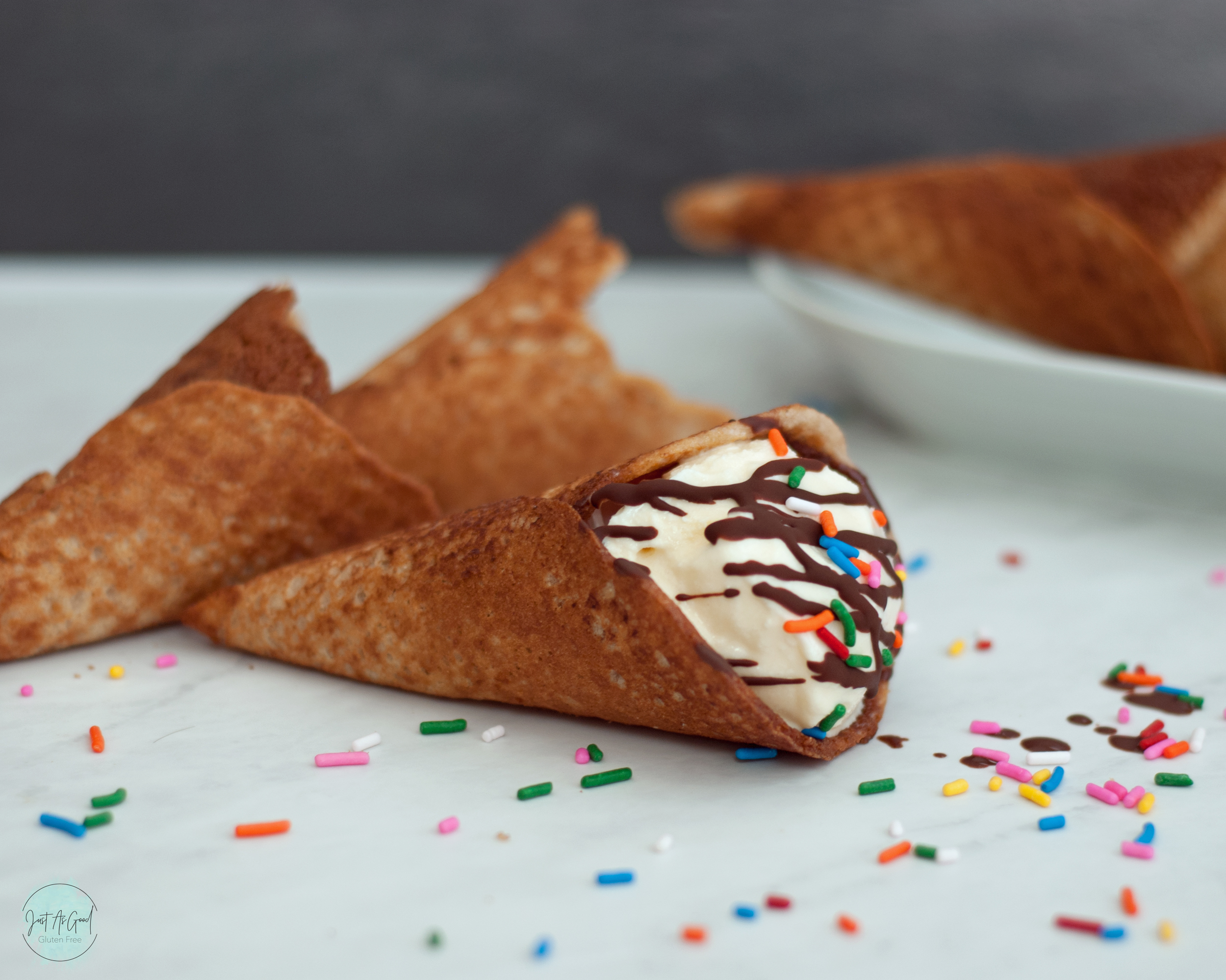 a waffle cone laying down with vanilla ice cream, chocolate drizzle and multi-colored sprinkles